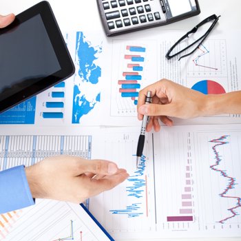 Foto eines Buchhalters, der mit einem Kunden über Finanzen spricht, der Tisch ist mit Finanzdiagrammen übersät.
